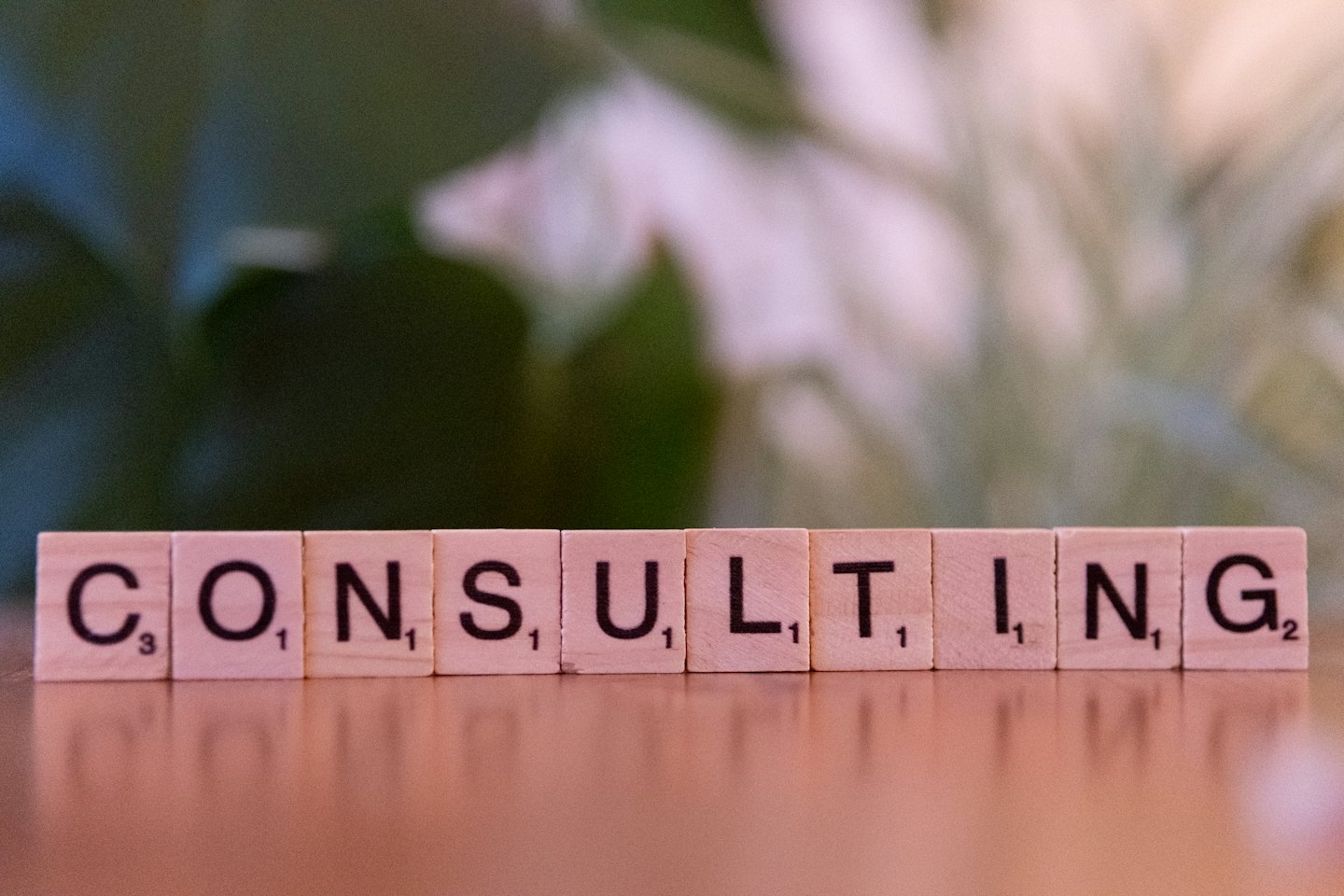 Scrabble tiles spell the word consulting on a wooden table.